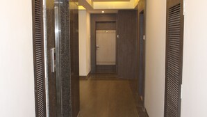 A hallway with a wooden door at the end, a metal door on the left, and a wooden door on the right. - Jai Malahar Residency (Panvel)