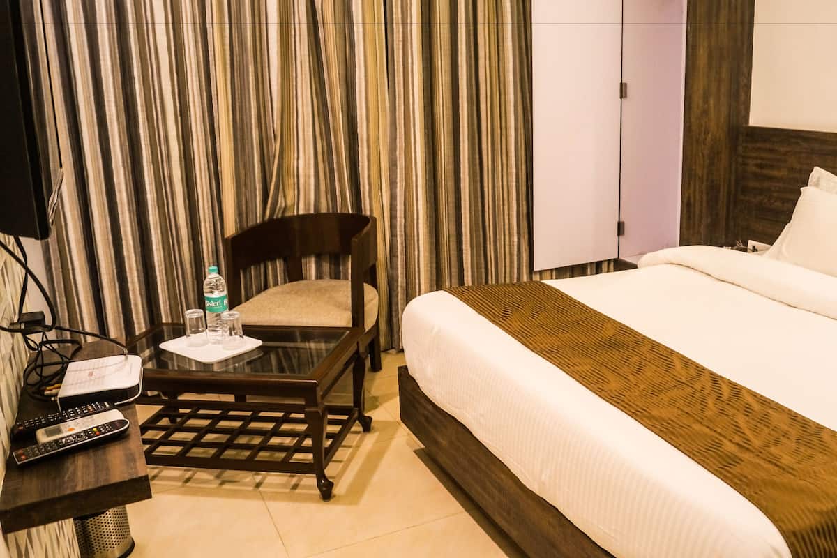 Une chambre d’hôtel avec un lit, une chaise, une table avec une bouteille et des verres, et un téléviseur.