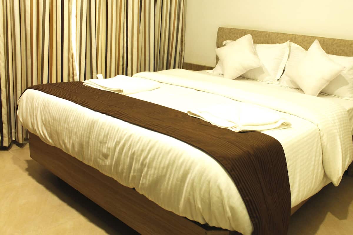 Une chambre d’hôtel avec un grand lit, une tête de lit en bois, du linge de lit blanc et une table de chevet dotée d’une prise électrique.