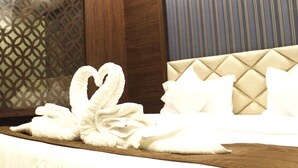 A hotel room with a bed featuring a tufted headboard, a decorative wall panel, and a neatly arranged set of towels. - Jai Malahar Residency (Panvel)