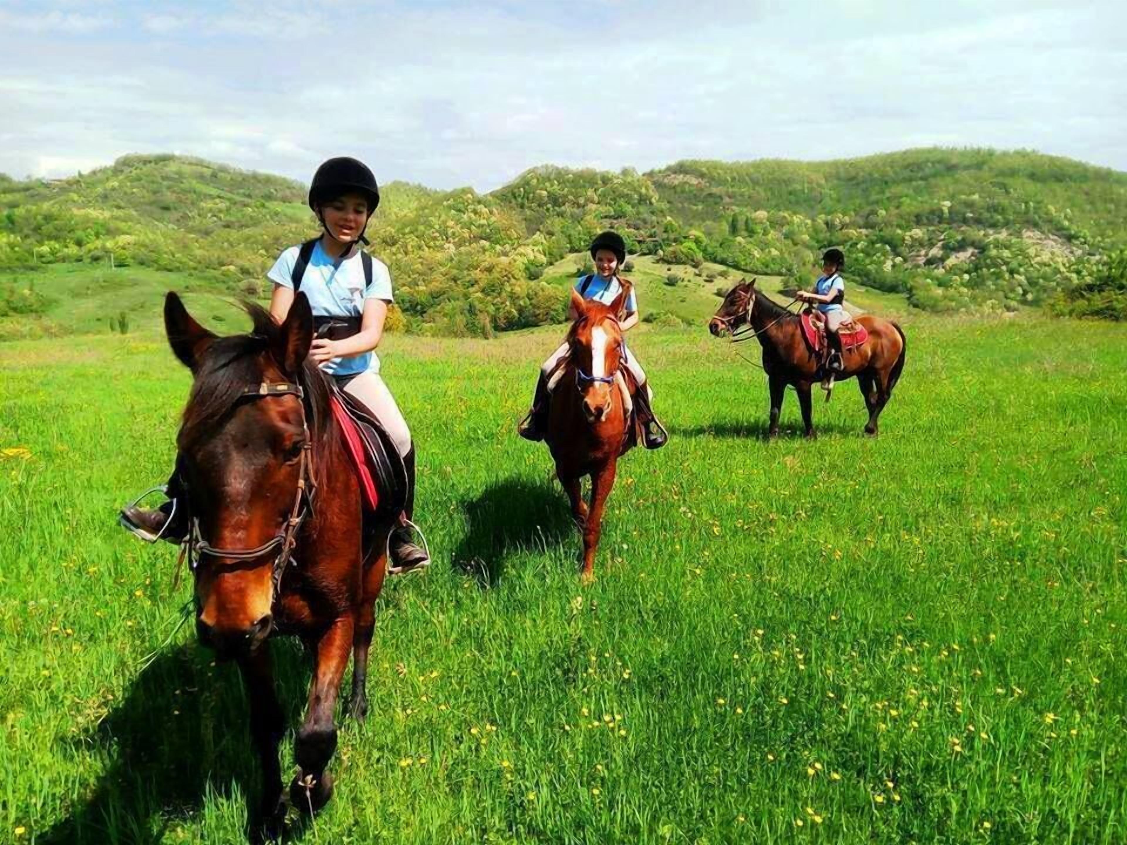 Tres personas montando a caballo en un campo con colinas al fondo.