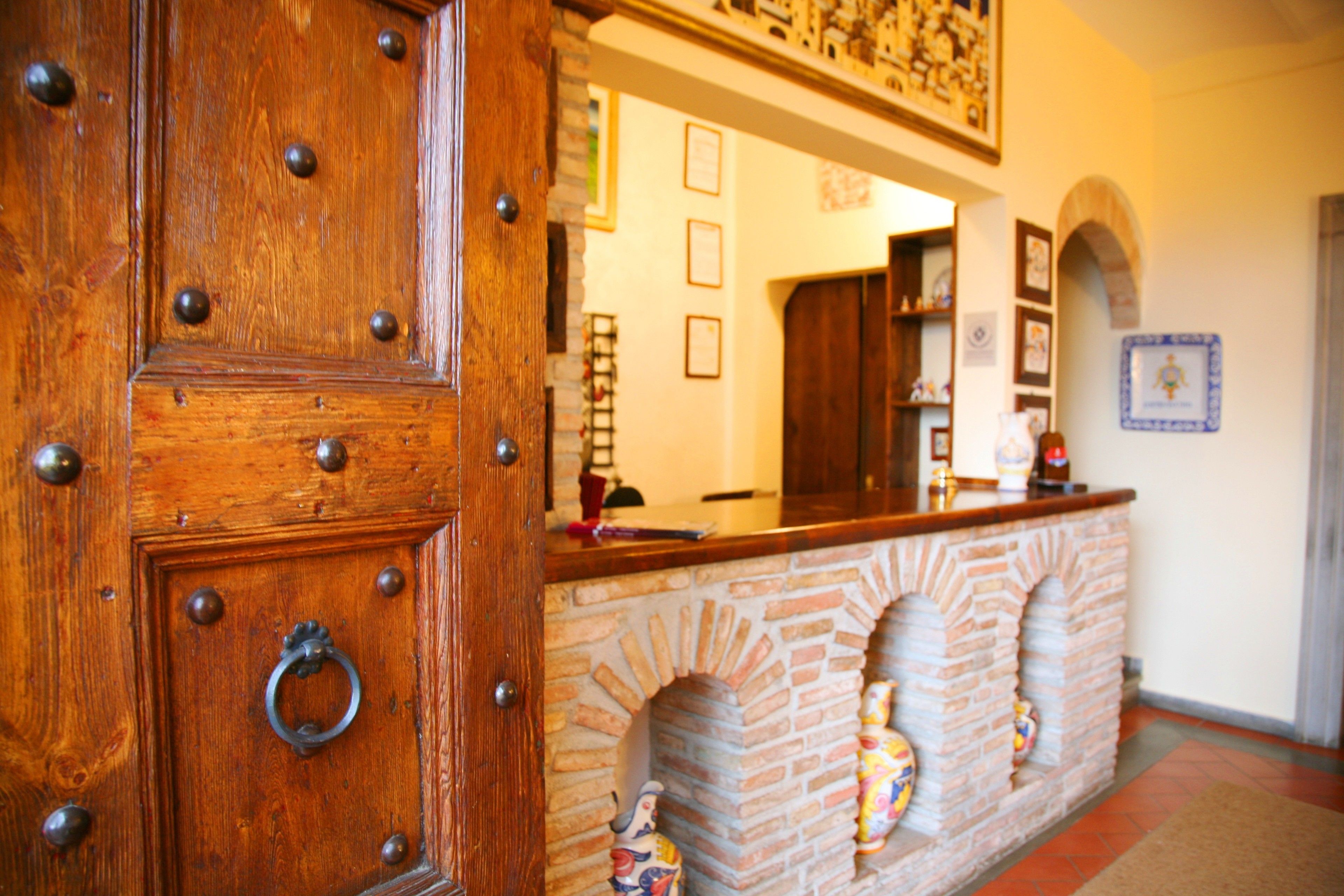 Una puerta de madera con remaches de metal y un tirador de anillo, una chimenea de ladrillo con figuras decorativas, y un mostrador con un espejo encima.