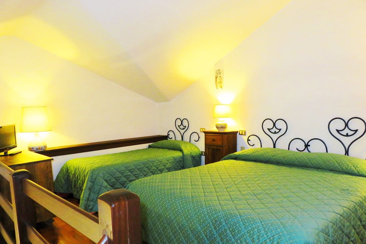 Una habitación con dos camas, cada una con ropa de cama verde, un cabecero de madera y una mesita de noche con lámpara.