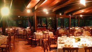 A spacious indoor dining area with multiple tables set for meals, wooden beams on the ceiling, and large windows allowing natural light. - Castello Cortevecchio (Gubbio)
