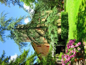A garden with a building, trees, and flowers.