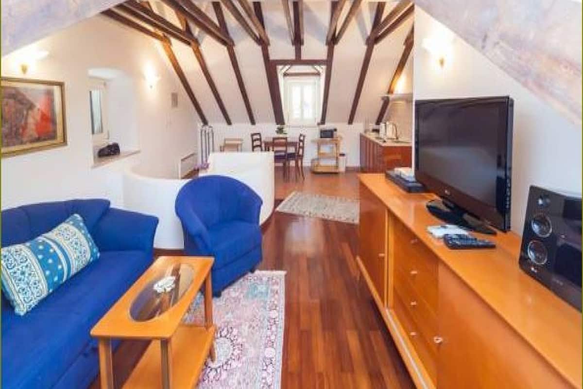 An attic room with a wooden ceiling, a TV, a sofa, a chair, and a dining area.