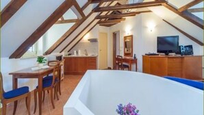 A high-ceilinged room with exposed wooden beams, a dining area with a table and chairs, a kitchenette, and a television on a cabinet. - Apartments Vi-La (Dubrovnik)