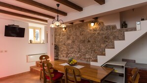 A dining area with a wooden table, red cushioned chairs, a fruit bowl, and a stone wall. - Apartments Vi-La (Dubrovnik)