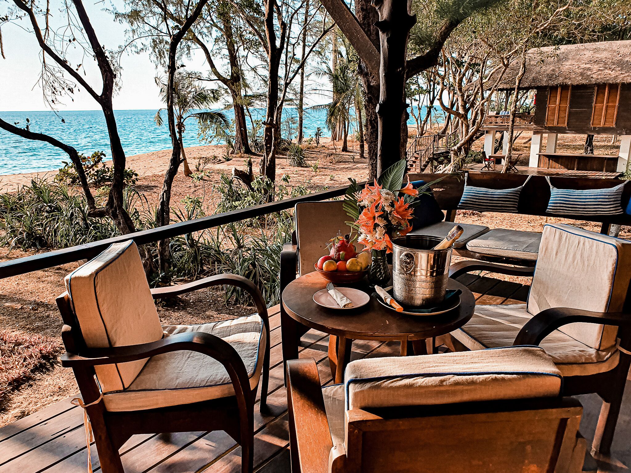 Eine Holzterrasse mit Gartenmöbeln mit Blick auf einen Strand und das Meer.