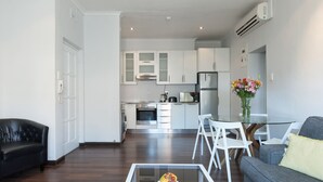 Un salon moderne avec une table basse en verre, un canapé et un coin repas avec des chaises blanches.