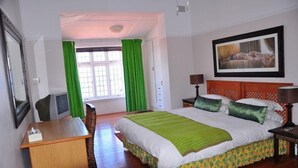 A hotel room with a bed, a desk, a chair, a TV, and a window with curtains. - Admirals Rest Self-Catering House (Mossel Bay)