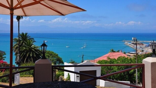 A coastal view with a clear sky, a white umbrella, and a few boats on the water. - Admirals Rest Self-Catering House (Mossel Bay)