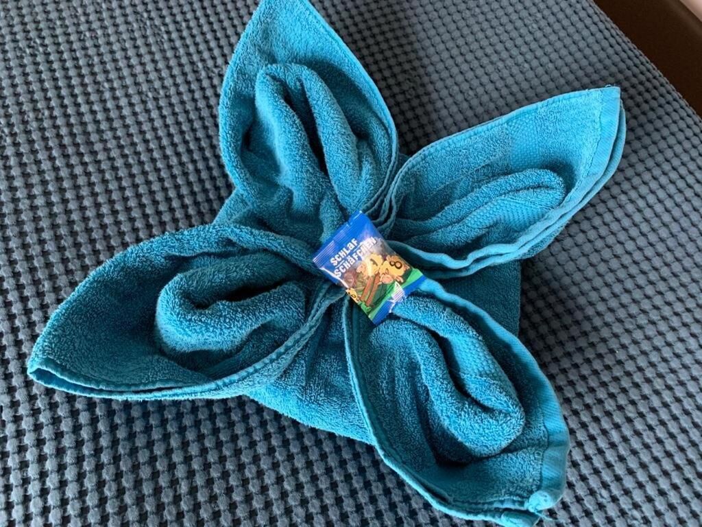 A blue towel folded into a flower shape with a small item attached in the center.