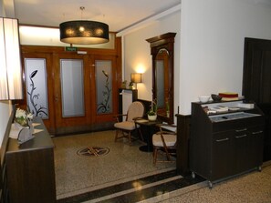 Eine Lobby mit einer Rezeption, einem Sessel, einem Tisch mit Blumenvase, einem Spiegel und einem Schrank.