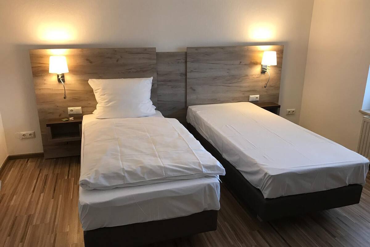 Habitación doble con dos camas individuales, cabeceros de madera, lámparas de noche y una mesita de noche con lámpara.