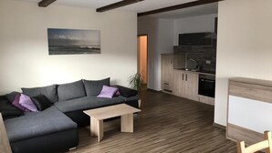 Una sala moderna con un sofá seccional gris, una mesita de centro de madera y un cuadro de un paisaje en la pared.