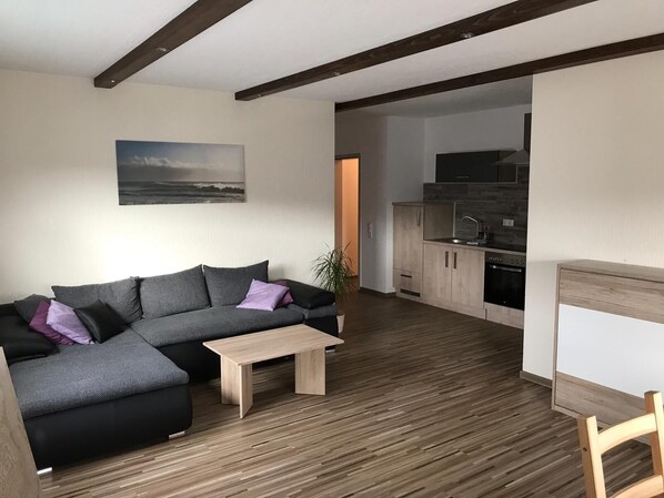 Una sala moderna con un sofá seccional gris, una mesita de centro de madera y un cuadro de un paisaje en la pared.