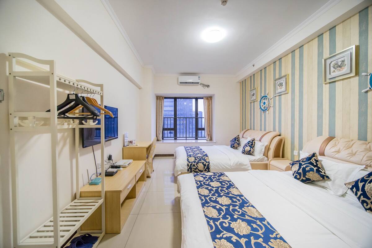 A hotel room with two beds, a desk, a chair, a TV, and a window with curtains.
