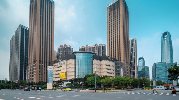 Un moderno skyline urbano con grattacieli, una piazza centrale e un edificio curvo, il tutto sotto un cielo azzurro limpido.