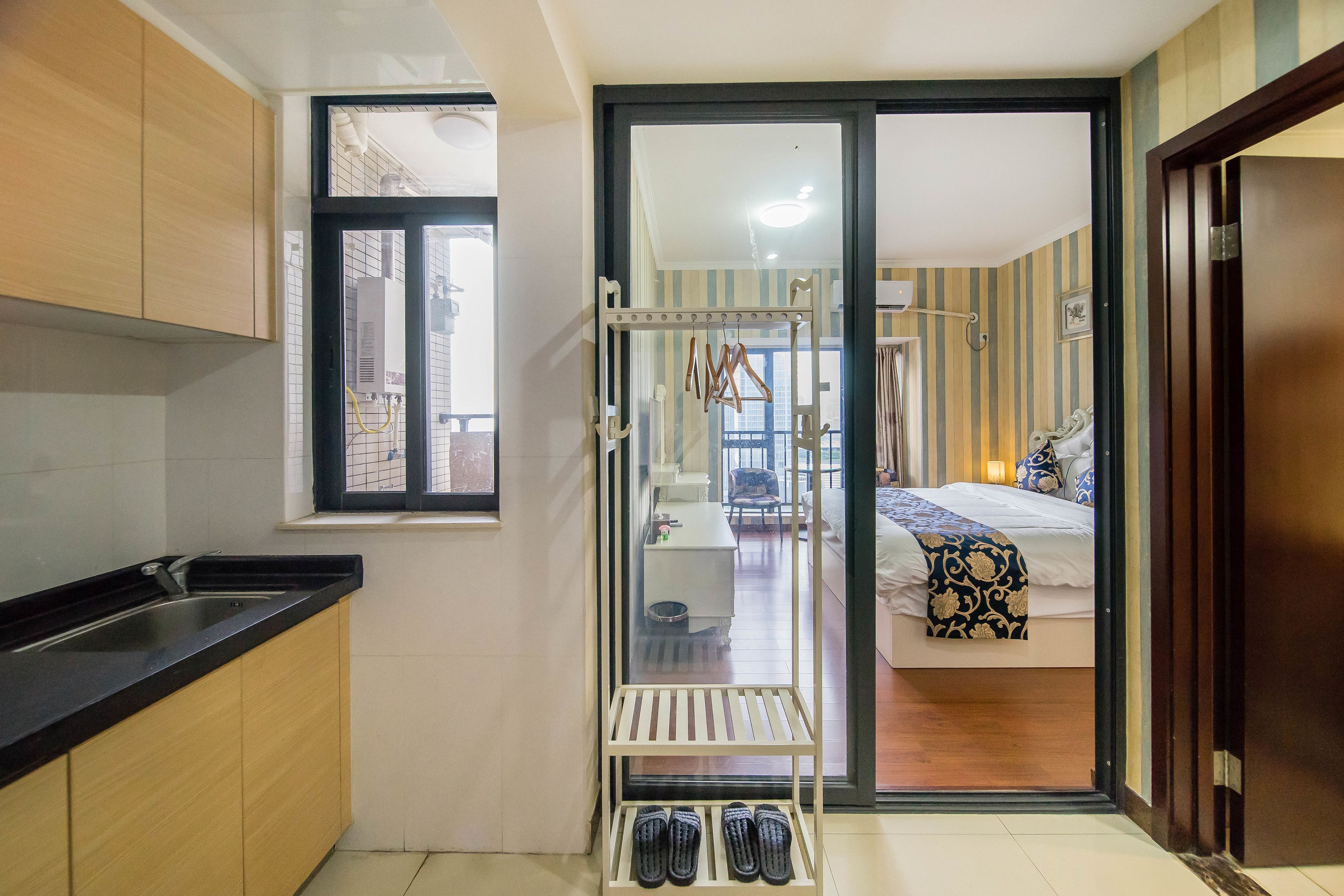 Cocina compacta con ventana, un zapatero y vistas a un dormitorio con cama y sillón.