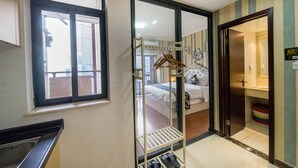 Una camera d'albergo con un letto, un appendiabiti, un bagno con lavandino e WC, e una finestra con vista all'esterno.