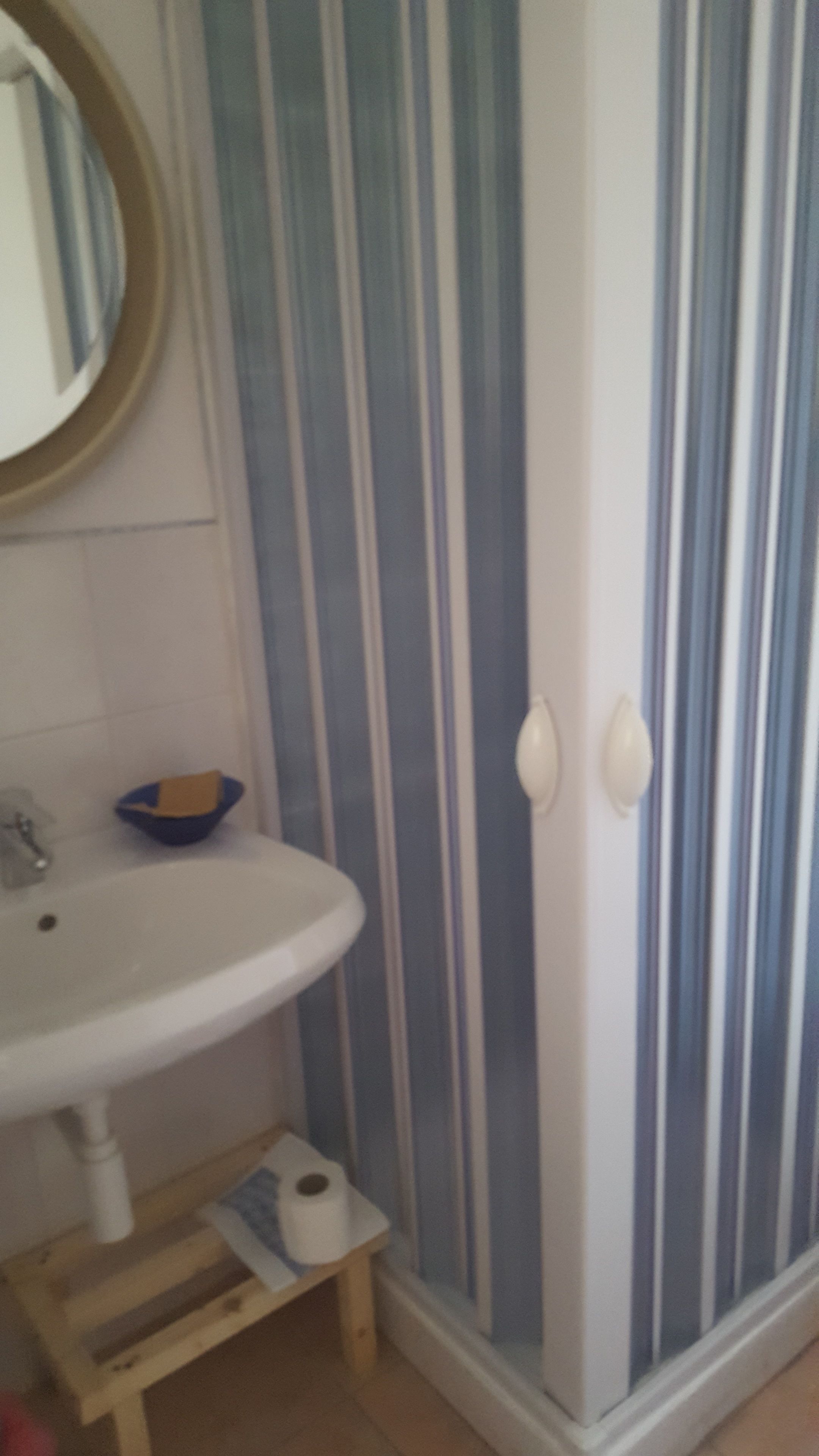 Een badkamer met een witte wastafel, een blauwe kom, gestreept behang en een houten kruk.