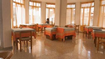 A dining area with tables and chairs, large windows with curtains, and a polished floor.