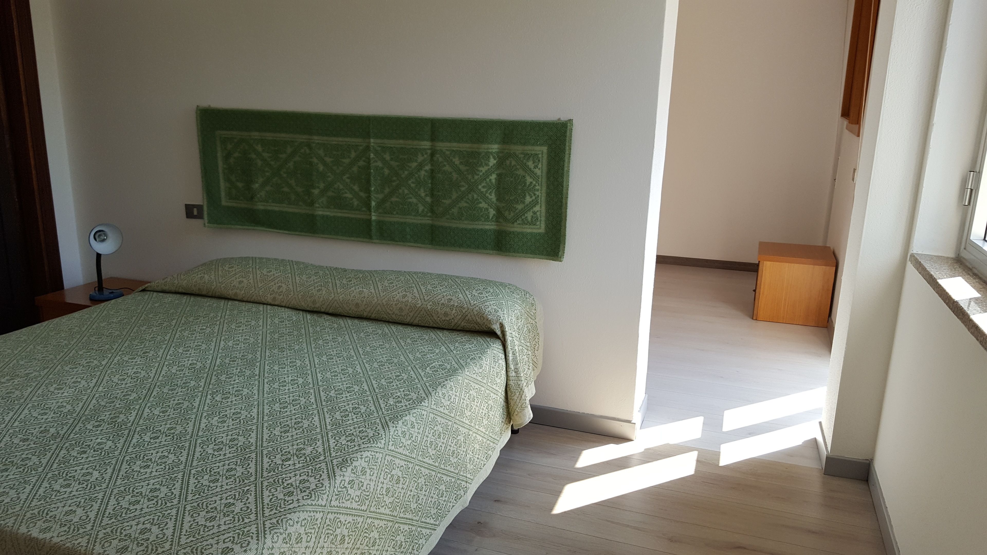 Une chambre à coucher avec un lit, un tapis à motifs verts, une lampe sur pied et une table de chevet en bois.