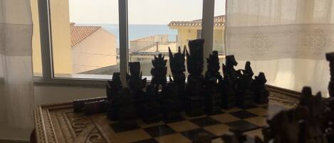 A chessboard with figurines in a room with a large window overlooking a building with a tiled roof.