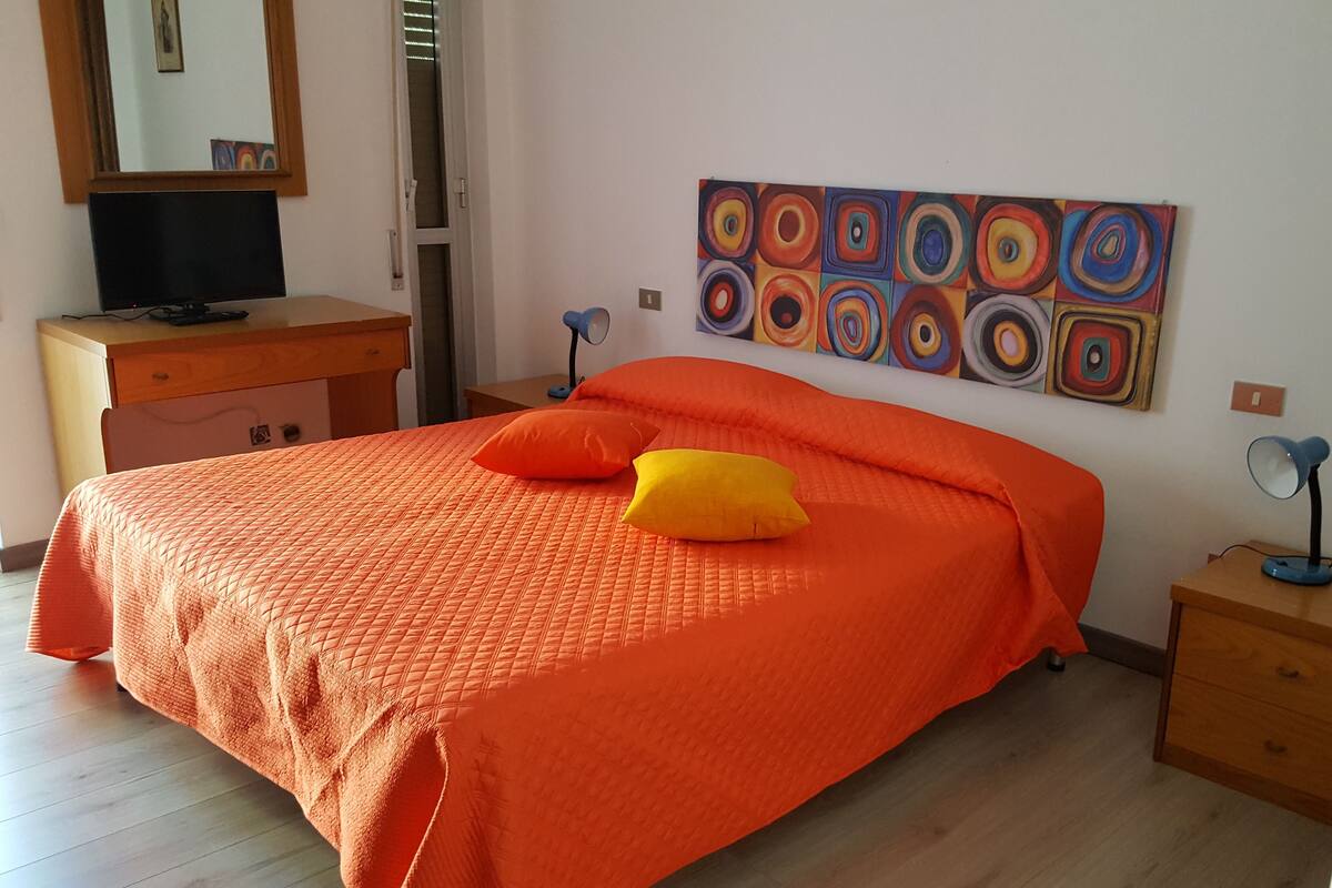 Una habitación con una cama, un escritorio, una silla, una lámpara y un cuadro en la pared.