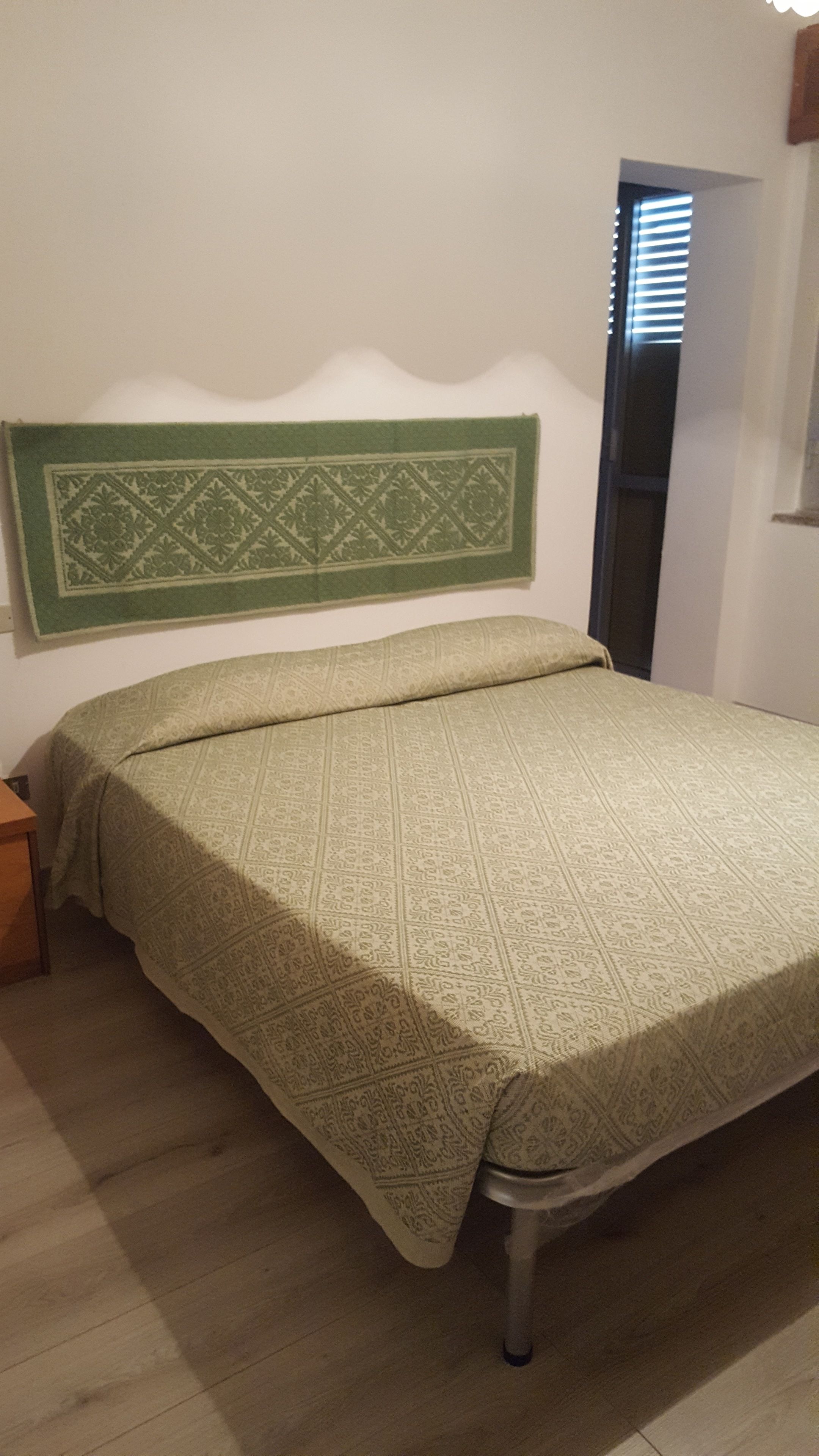 Una cama con una colcha estampada, un cabecero con diseño geométrico y una mesita de noche de madera a la izquierda.
