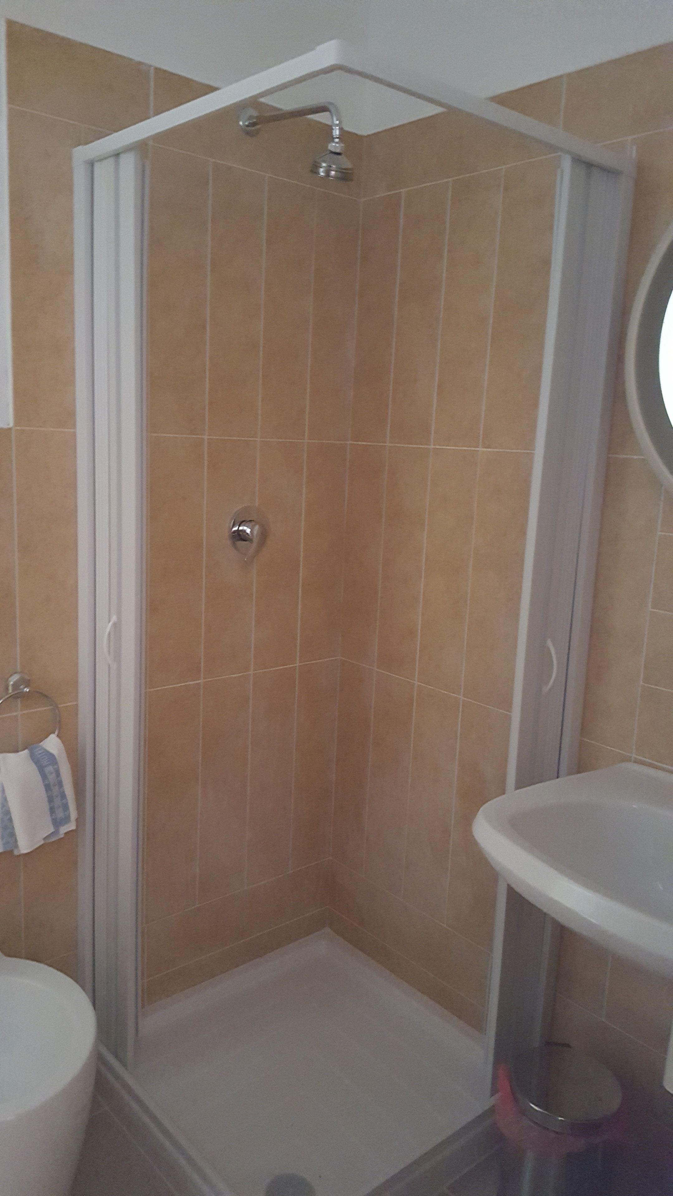 Ducha con puerta de vidrio, lavamanos blanco y un perchero para toallas.