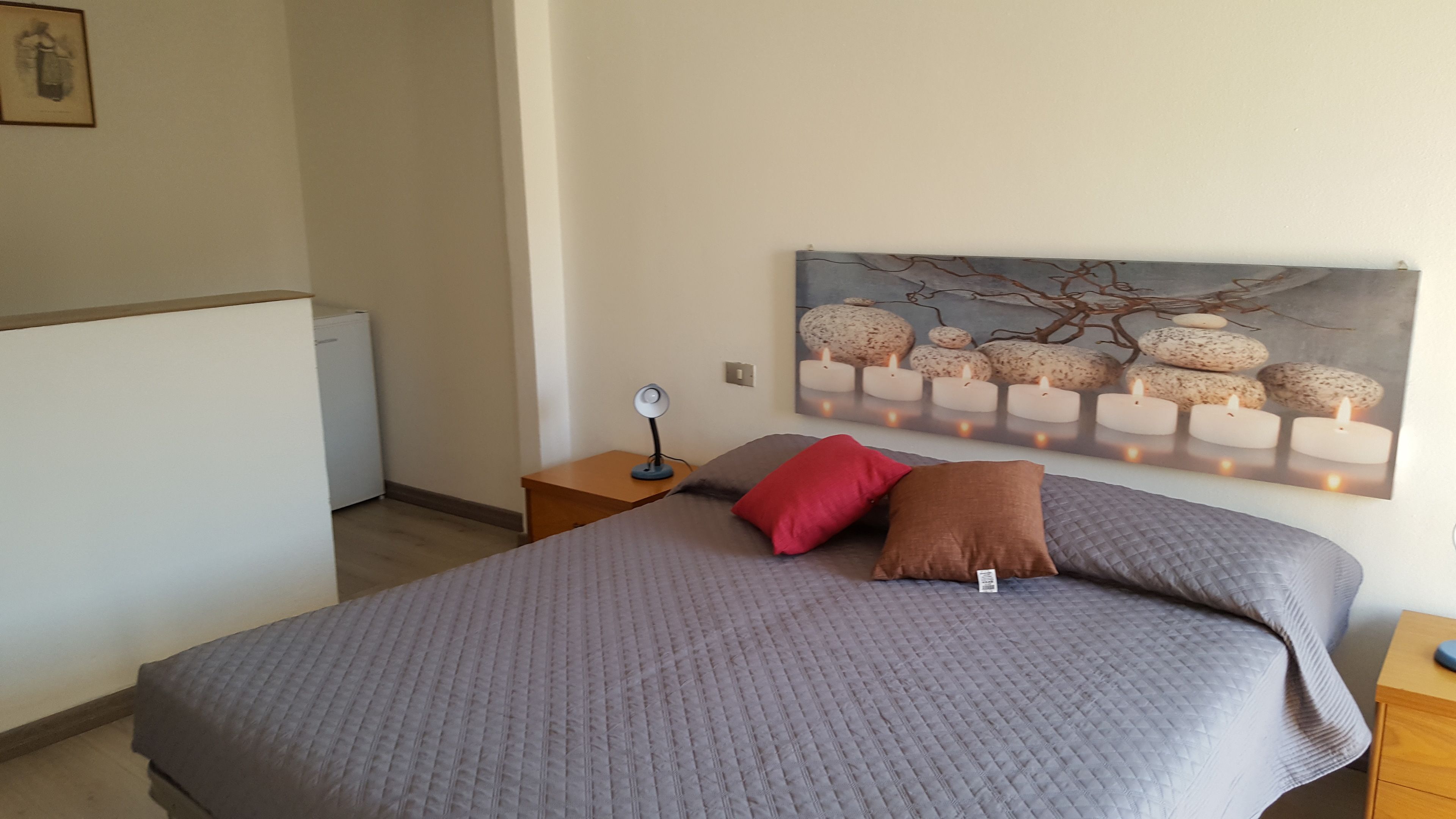 Un dormitorio con cama, mesita de noche, lámpara de pared y un cuadro de piedras y velas.