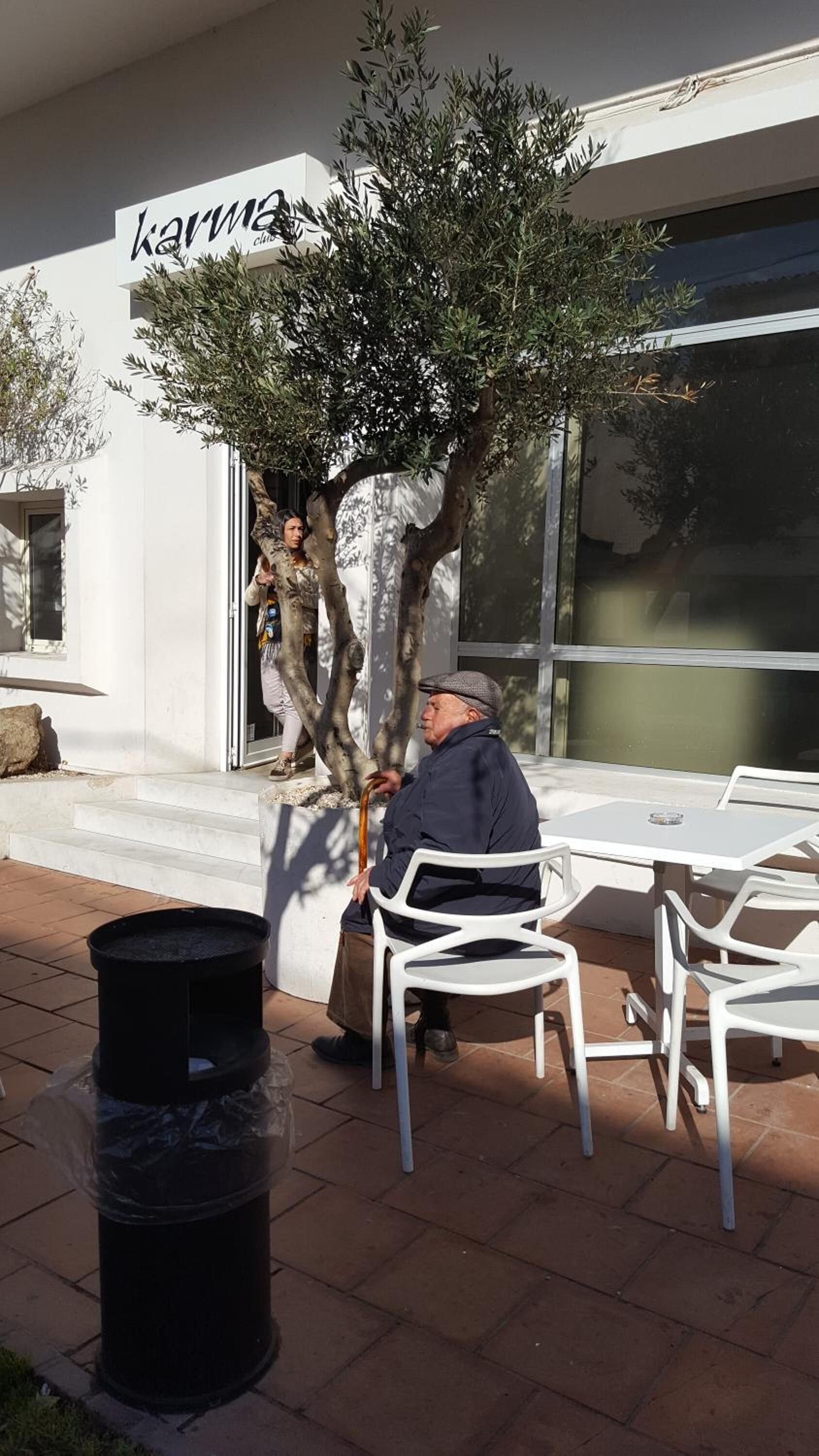 An outdoor seating area with white plastic chairs and a trash bin.