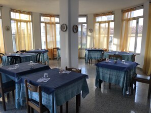 A dining area with tables set for two, featuring blue tablecloths and wooden chairs. - Hotel L'Ancora (Siniscola)