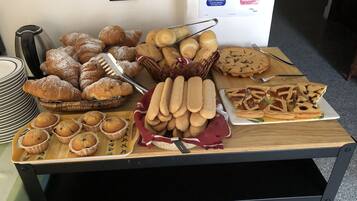 A buffet table with various baked goods including pastries, muffins, and cookies.