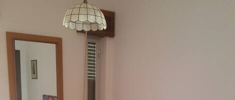 A bedroom with a bed, a desk, a chair, a lamp, a mirror, and a painting on the wall.