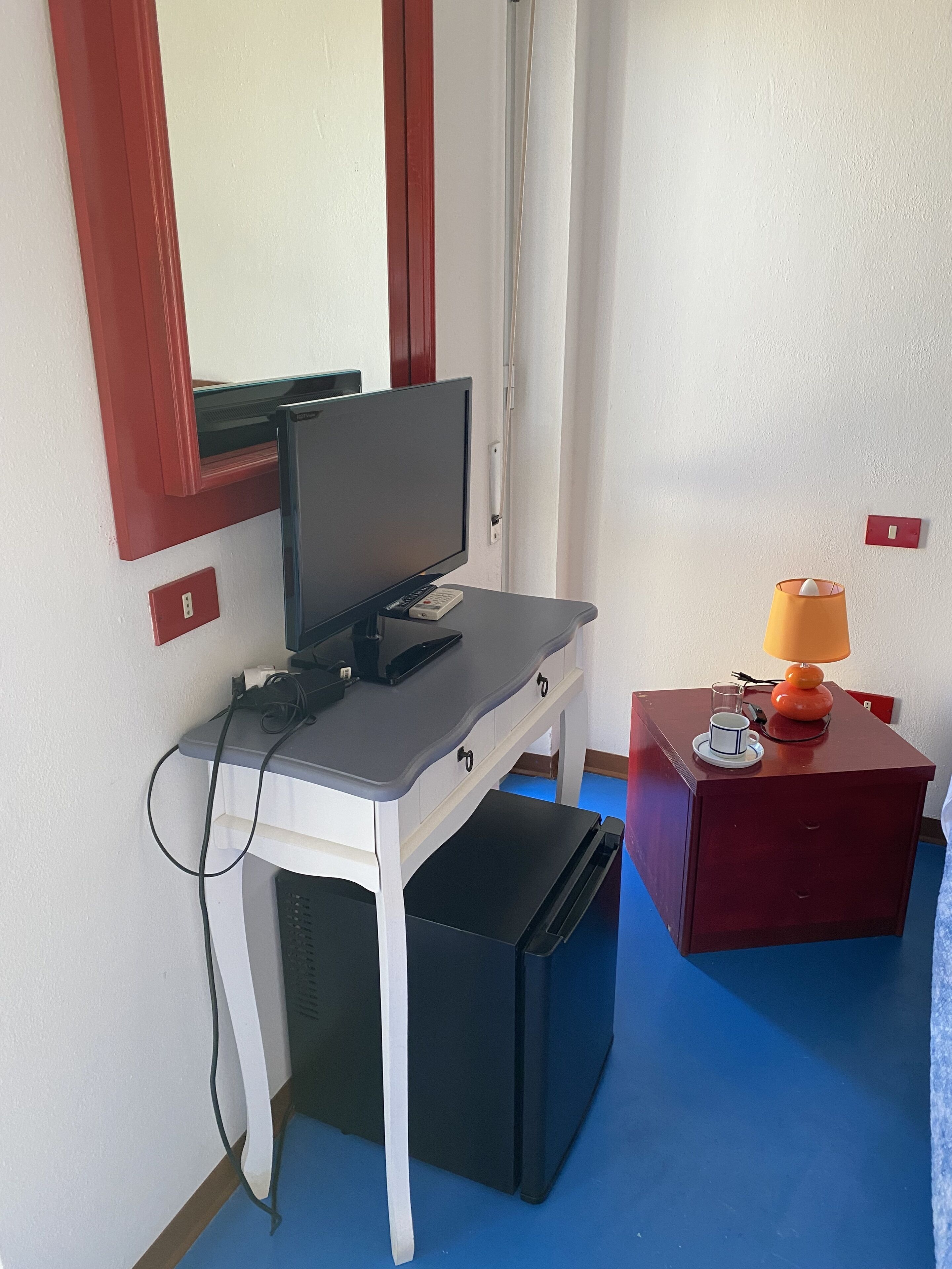 A room with a desk, a computer, a lamp, and a small refrigerator.