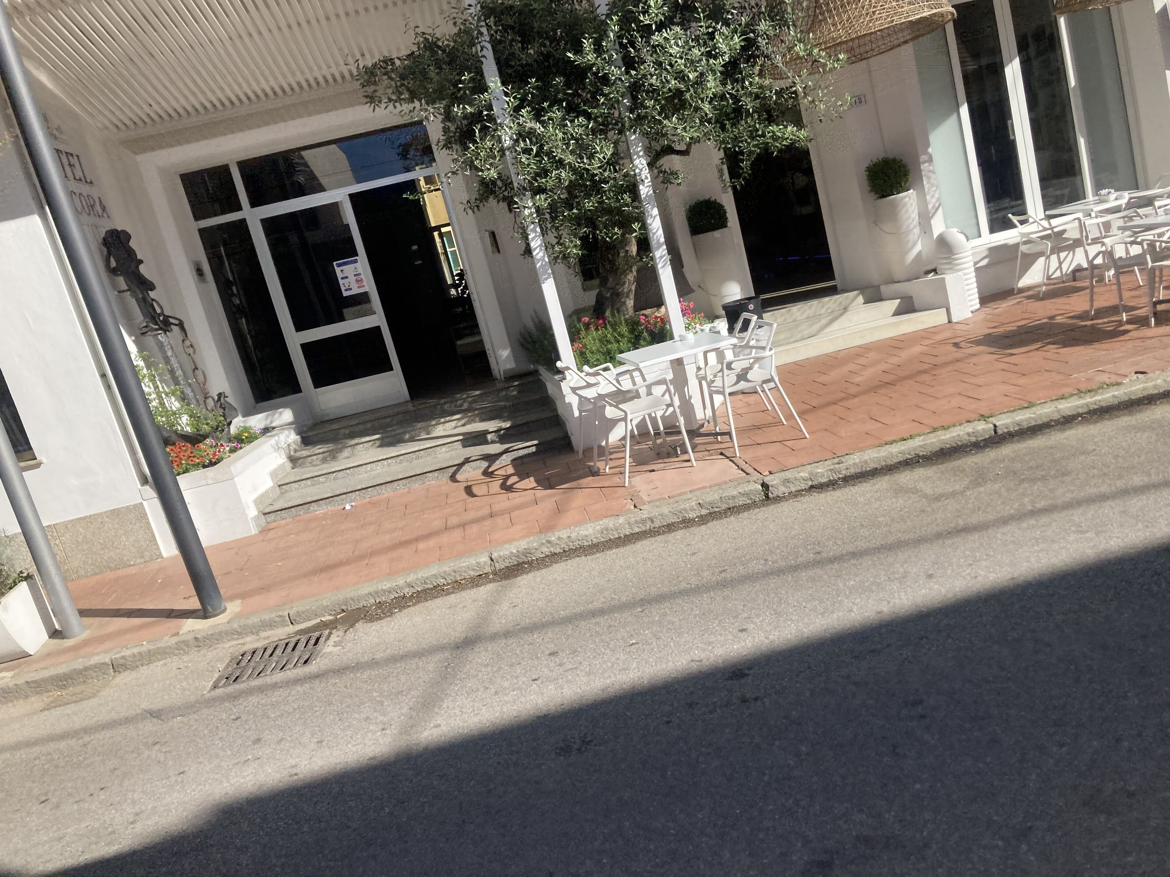 A building with a white facade, a set of outdoor tables and chairs, and a tree in front.