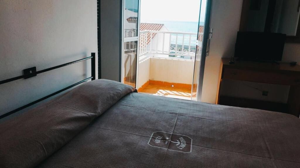 A bedroom with a bed, a window, and a balcony with a view of the sea.