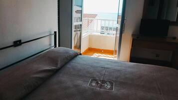 A bedroom with a bed, a window, and a balcony with a view of the sea.