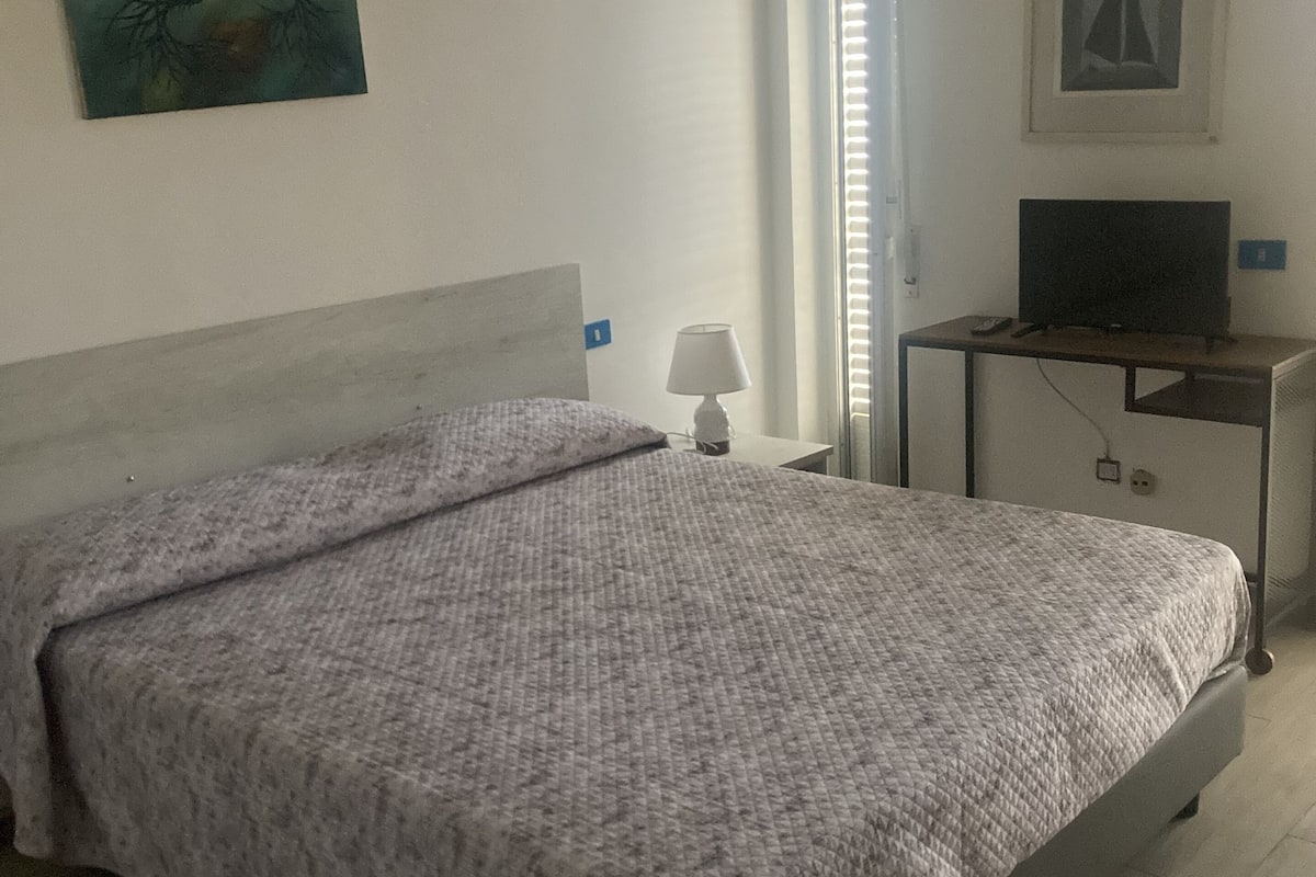 Un dormitorio con cama, mesita de noche, lámpara, televisor y obras de arte en las paredes.