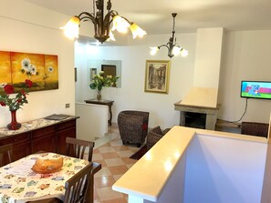 A living room with a fireplace, a dining area with a table and chairs, a TV mounted on the wall, and a chandelier. - Magralù B&B (Alghero)