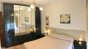 Una habitación de hotel con cama, mesitas de noche, un espejo grande y obras de arte colgadas en la pared.