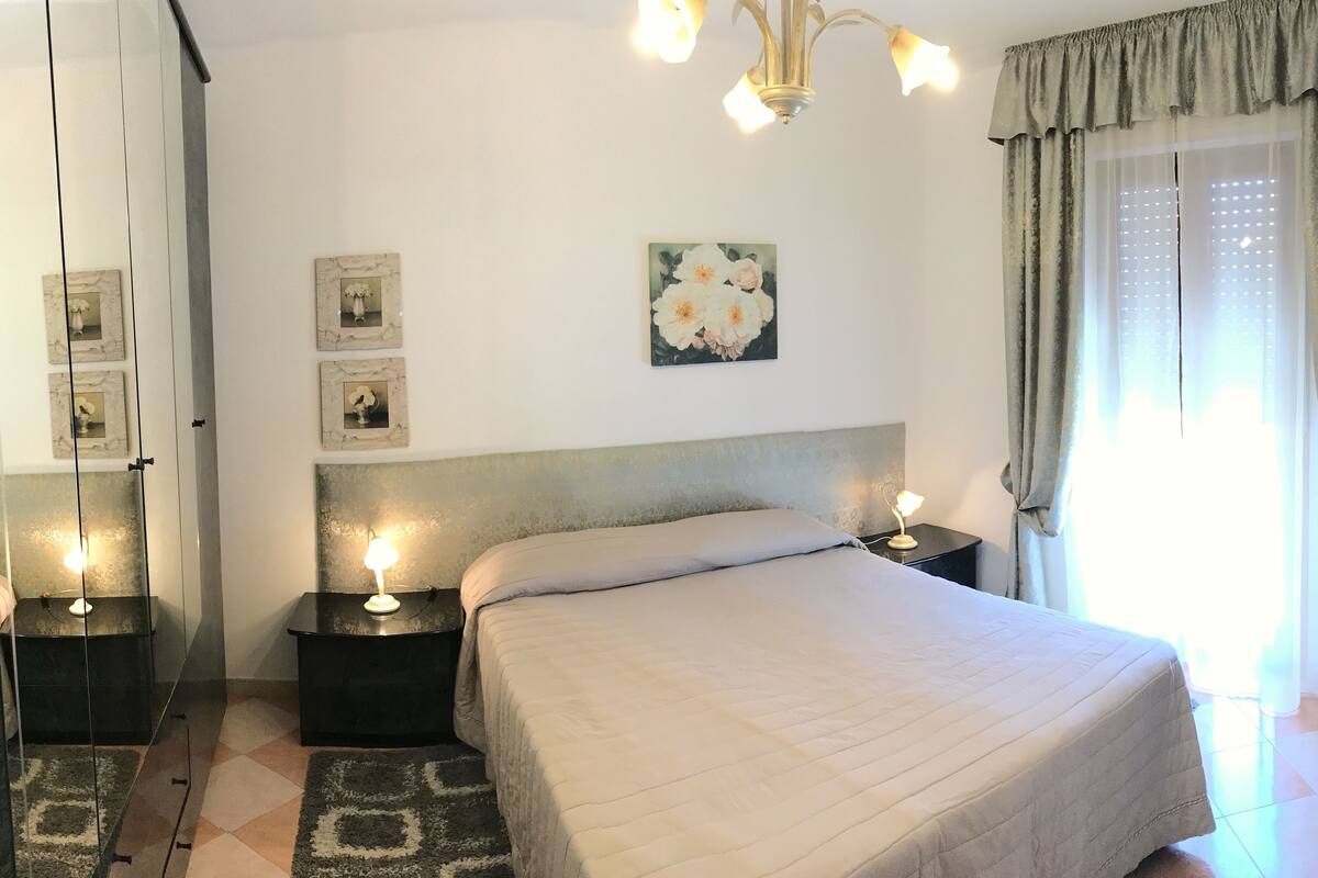 Une chambre à coucher avec un grand lit, des lampes de chevet, un lustre et une fenêtre avec des rideaux.