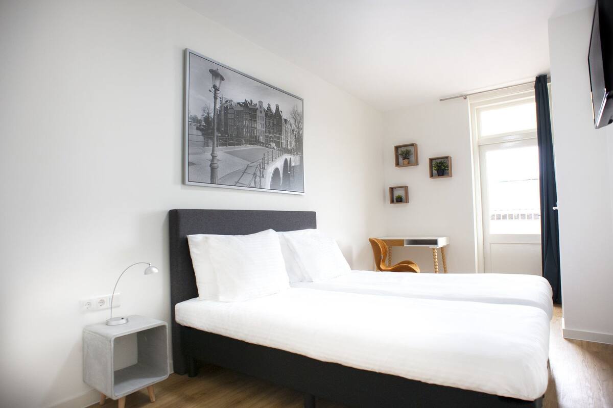A hotel room with a large bed, a desk, a chair, a lamp, and a picture on the wall.