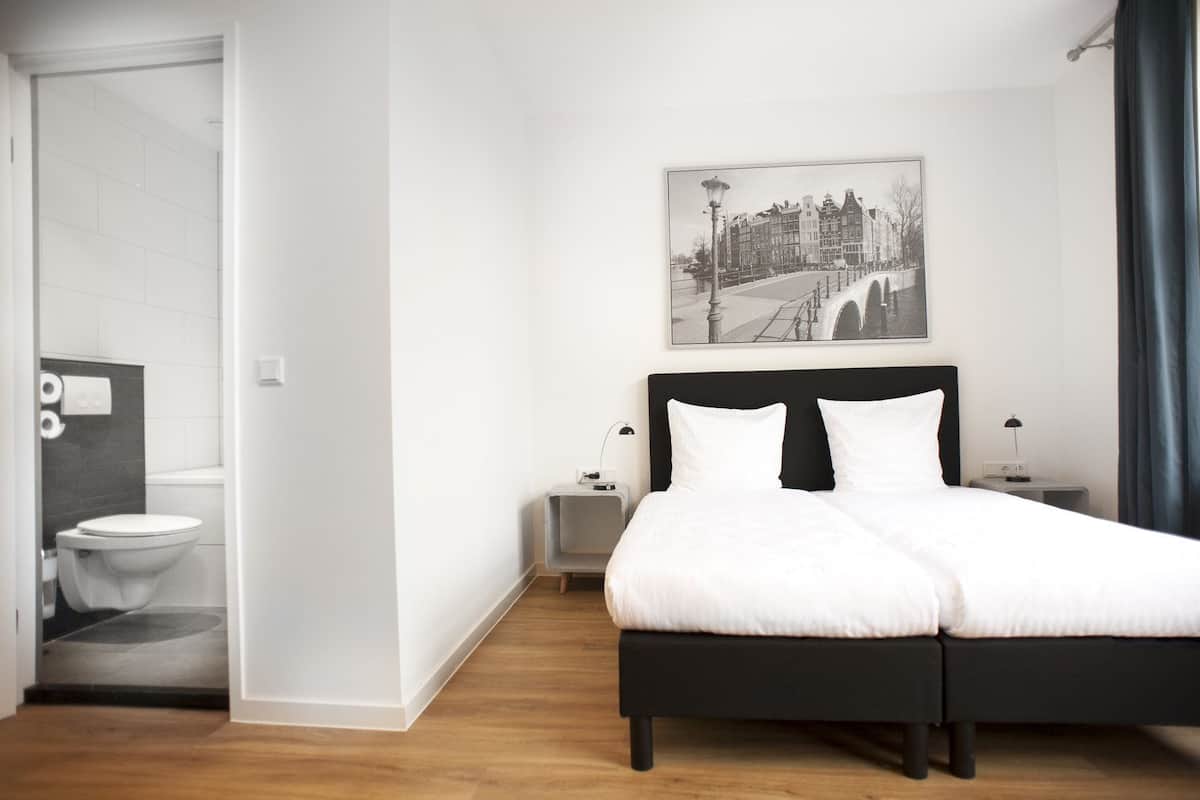 A modern hotel room with a large bed, a nightstand, a bedside table, and a picture of a cityscape on the wall.