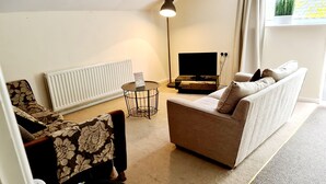A living room with a sofa, a coffee table, a floor lamp, and a television.