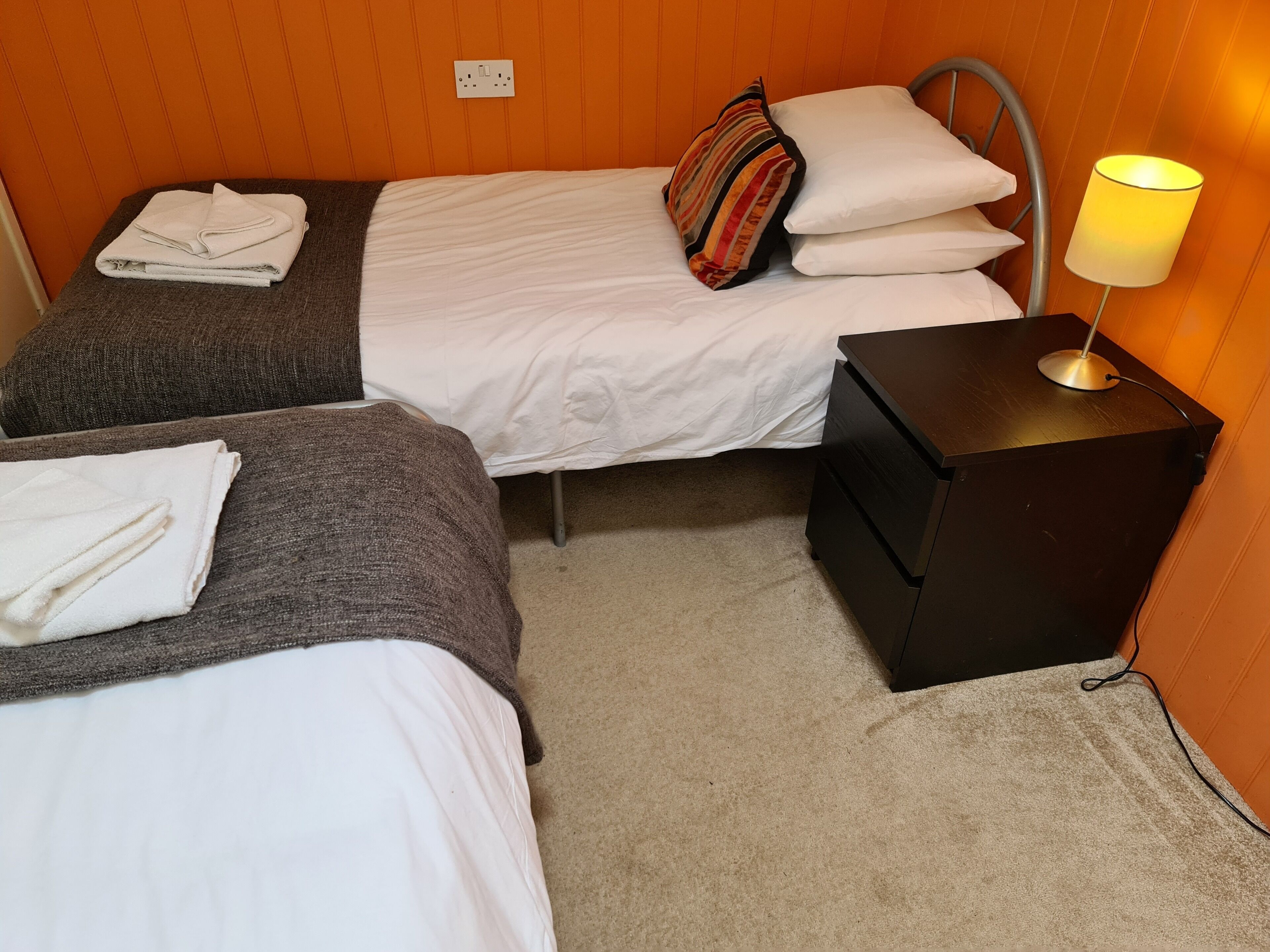 A hotel room with two beds, a nightstand, and a lamp.