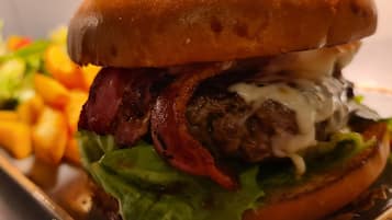 A close-up of a burger with a sesame seed bun, bacon, lettuce, and a creamy sauce.